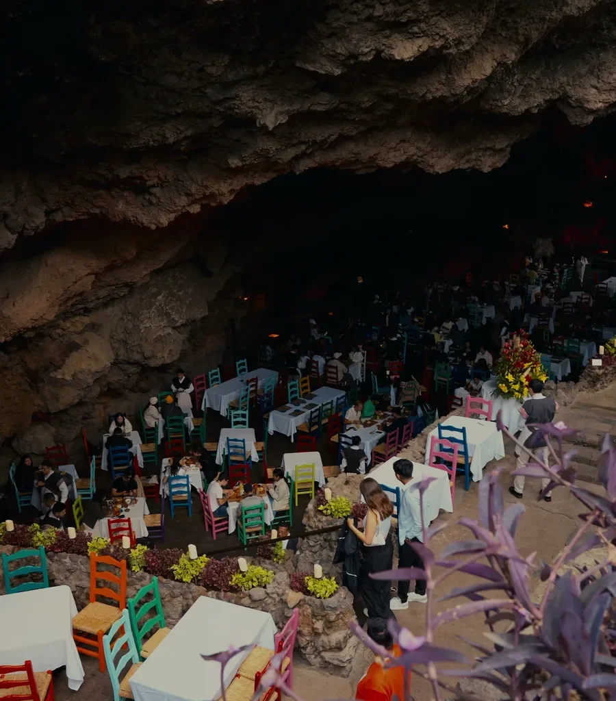 Vuelo en globo Teotihuacán + Desayuno en La Gruta 2 Mesas con mantel blanco y sillas pintadas de colores ocupan la gruta natural del restaurante La Gruta en Teotihuacán
